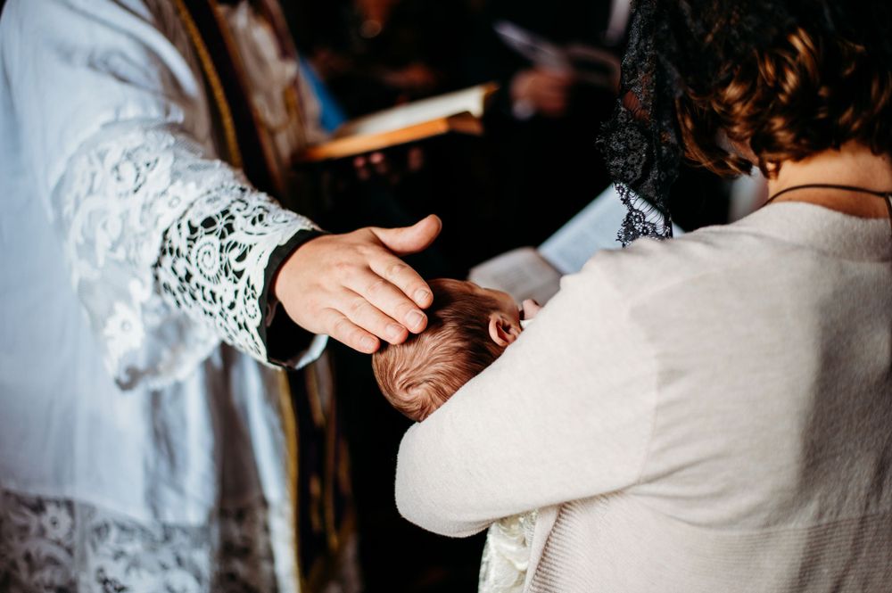 A young baby is blessed by the hand of a Catholic priest before receiving the Sacrament of Baptism in a Cathedral in St. Louis, MO.