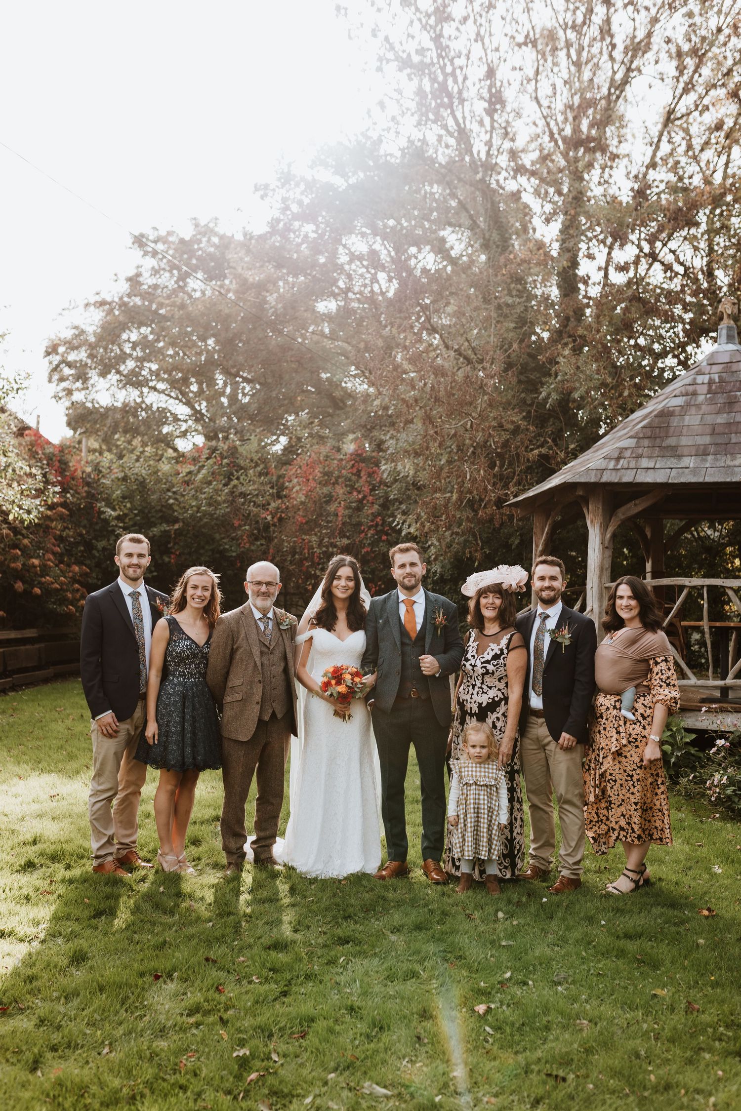 Wedding party stands together on grassy hill during outdoor autumn celebration.