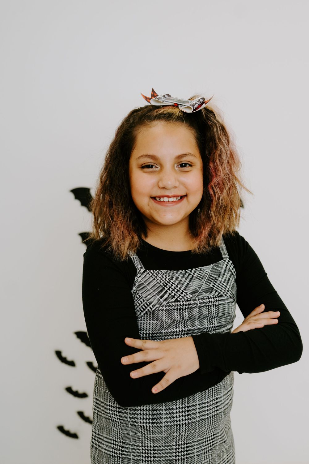 A Halloween-themed portrait featuring a plaid dress, black sweater, and decorative bats on the wall.