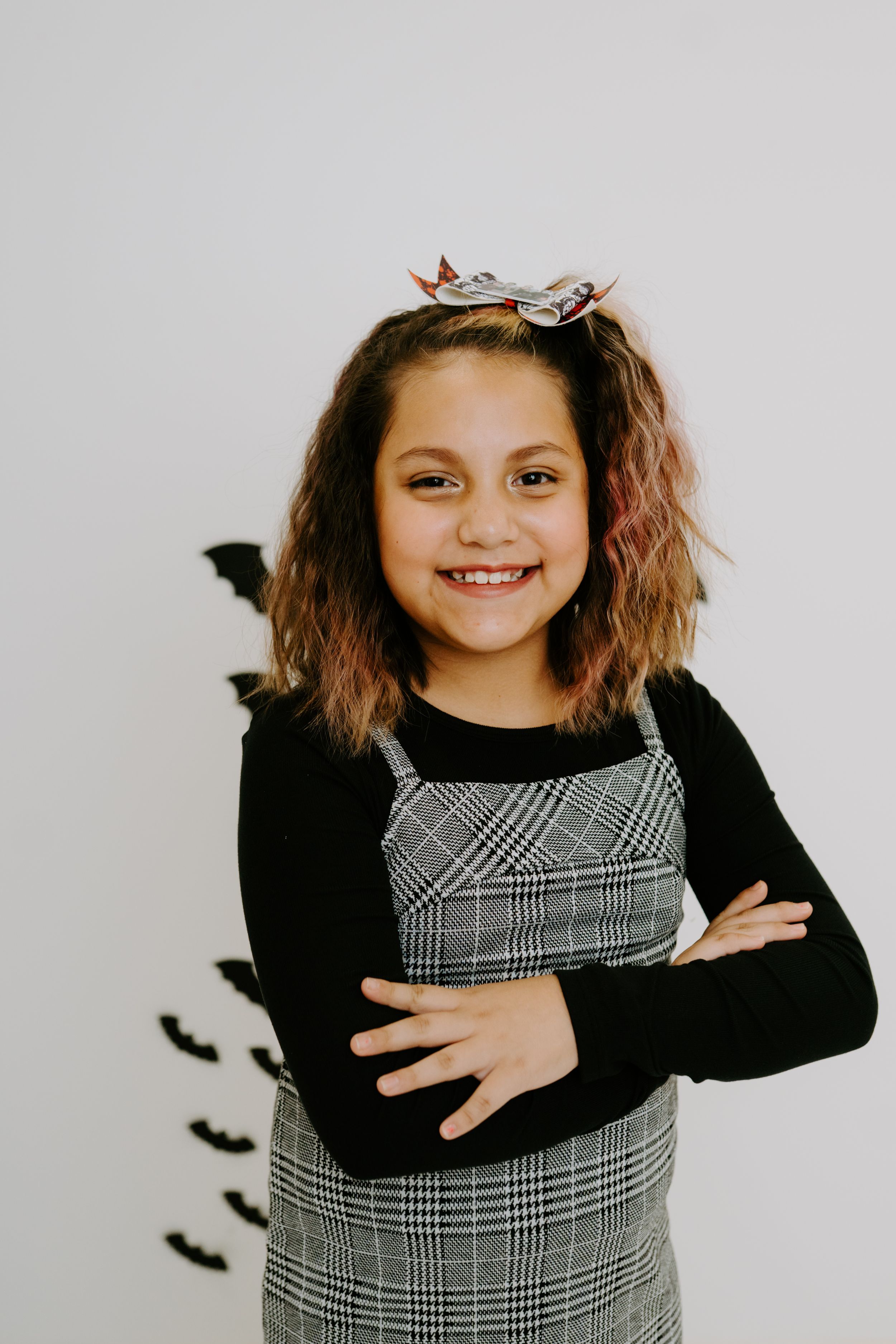 A Halloween-themed portrait featuring a plaid dress, black sweater, and decorative bats on the wall.