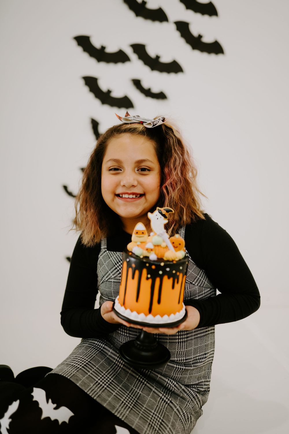 A Halloween scene with an orange drip cake and spooky bat decorations on the wall.