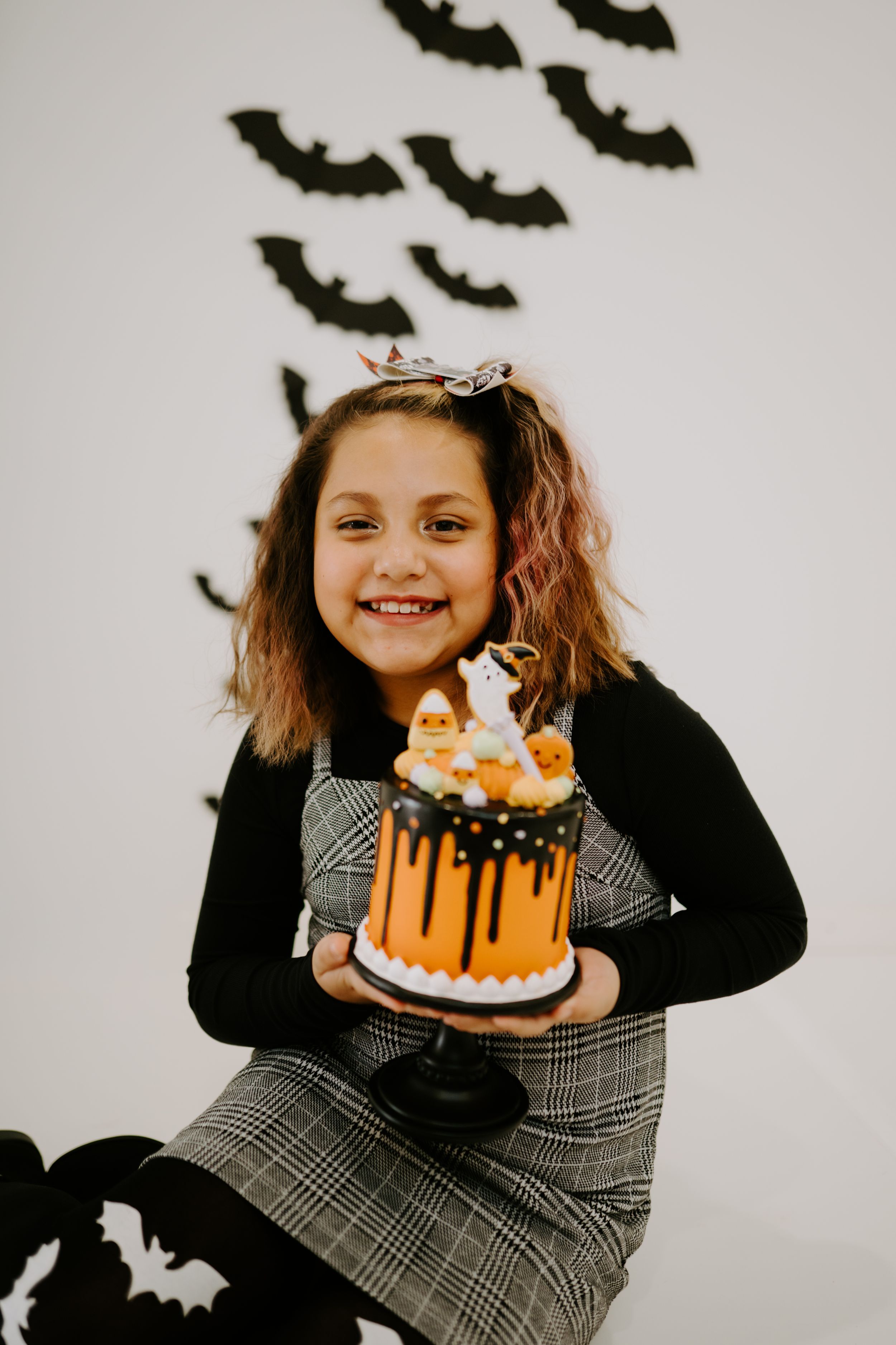 A Halloween scene with an orange drip cake and spooky bat decorations on the wall.