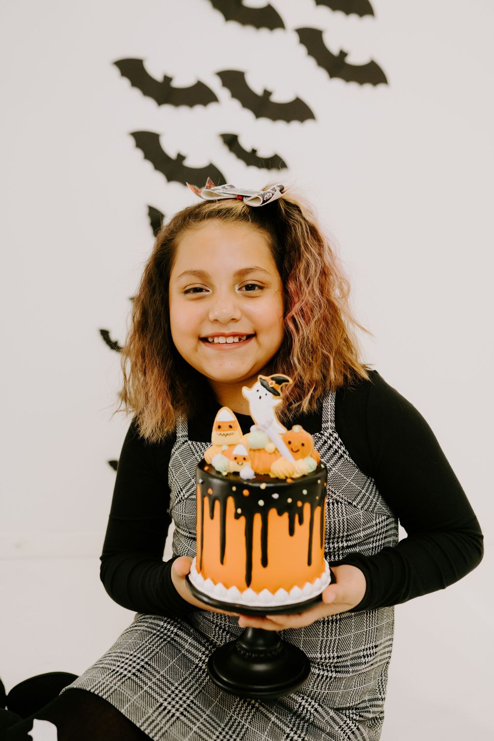 A Halloween-themed photo session with an orange cake and decorative black bats.