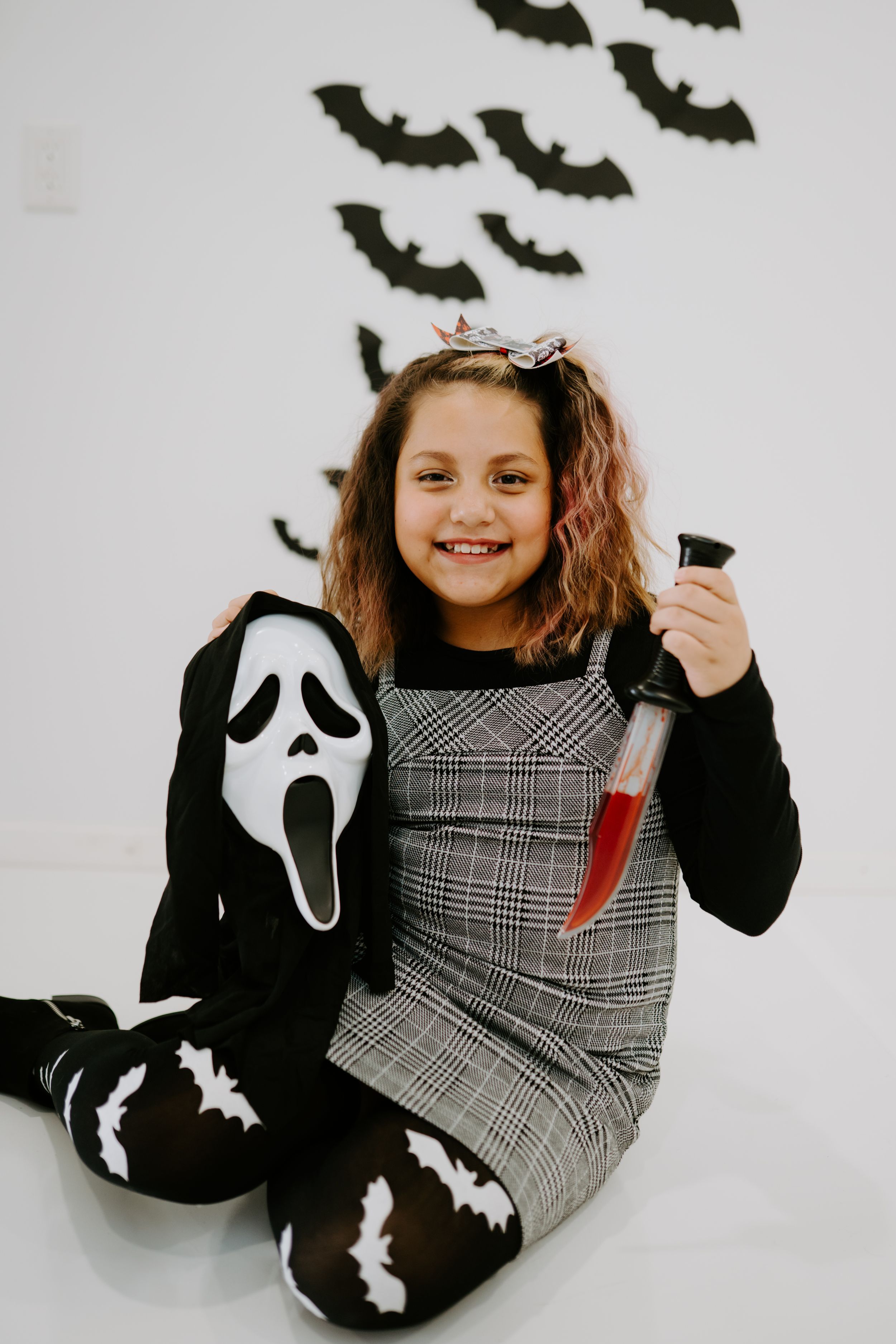 A Halloween portrait with a Scream mask and plaid dress against a white background.