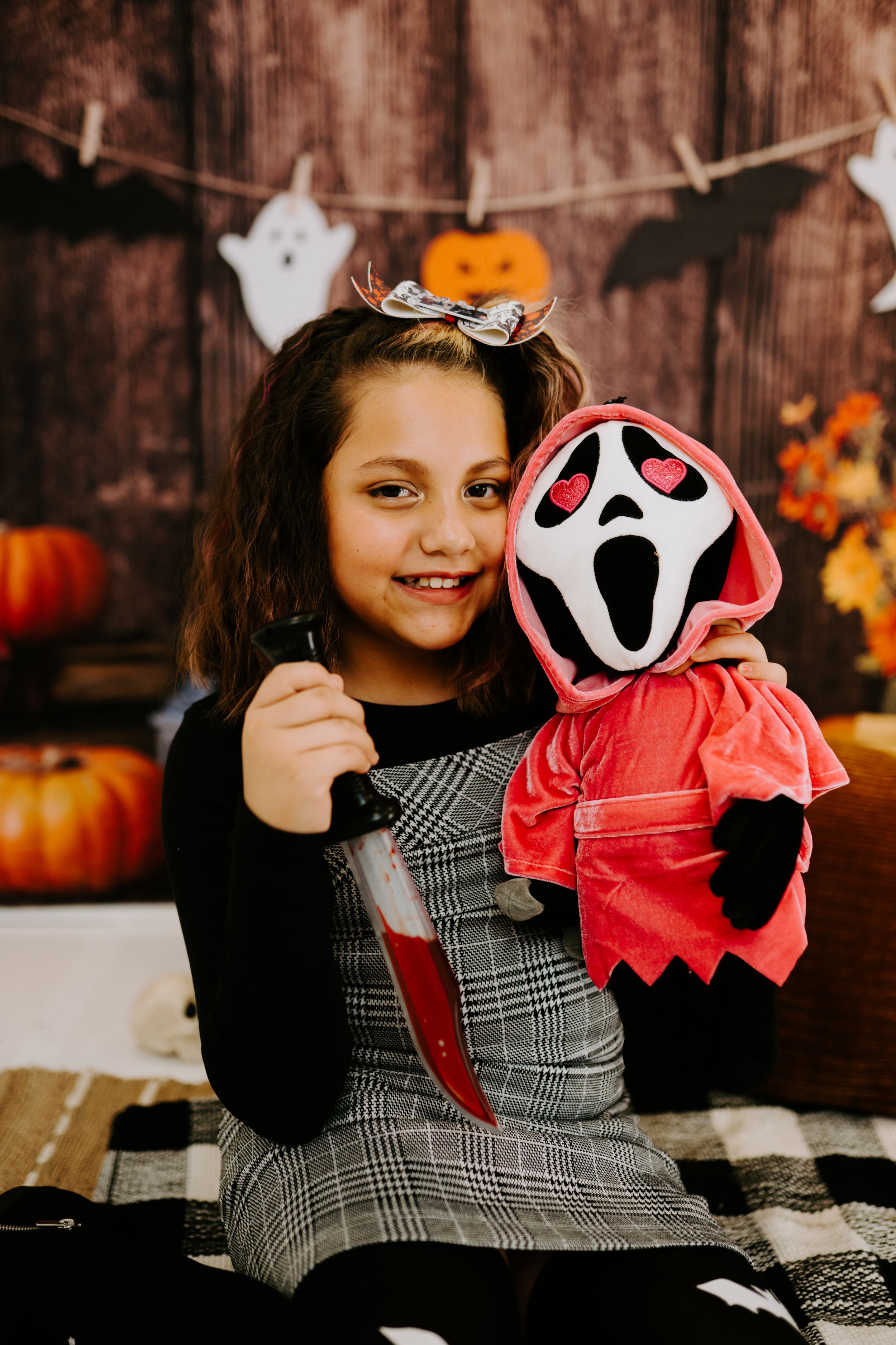 A Halloween photo with ghost plush, pumpkins, and autumn decorations against wooden backdrop.