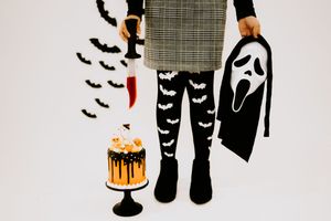 Halloween costume scene with plaid dress, Ghostface mask, knife and spooky decorated cake.