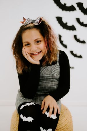 Young person in plaid dress and bat leggings poses with Halloween decorations.
