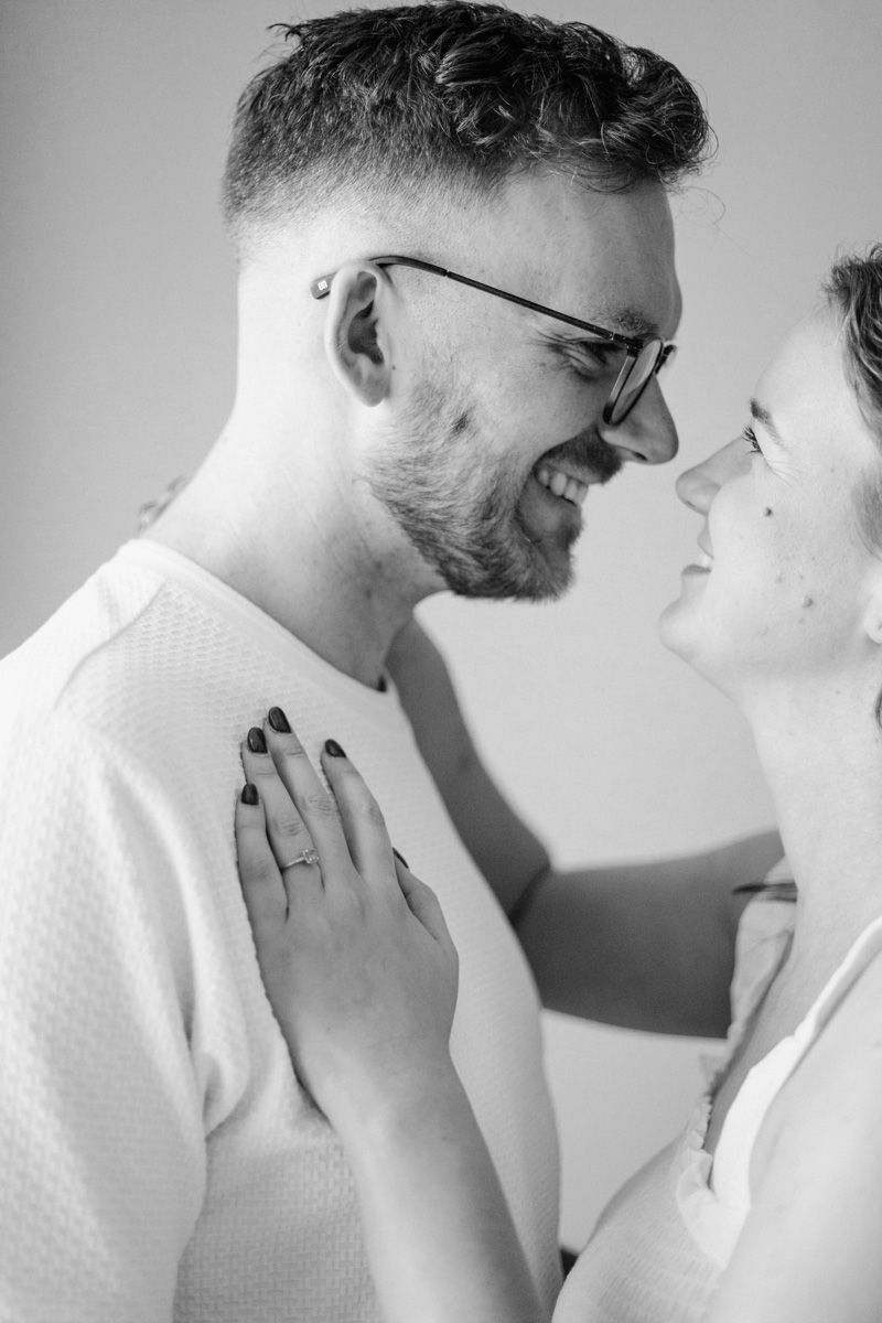 Black and white intimate portrait of a couple sharing a tender moment, with one wearing glasses and a white sweater.