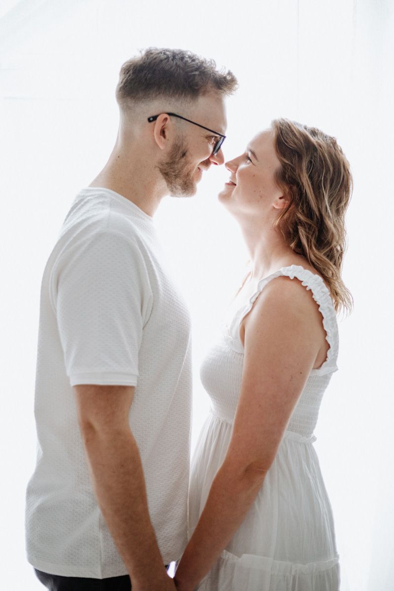 A romantic couple in white outfits shares an intimate moment against a bright background in a series of poses.