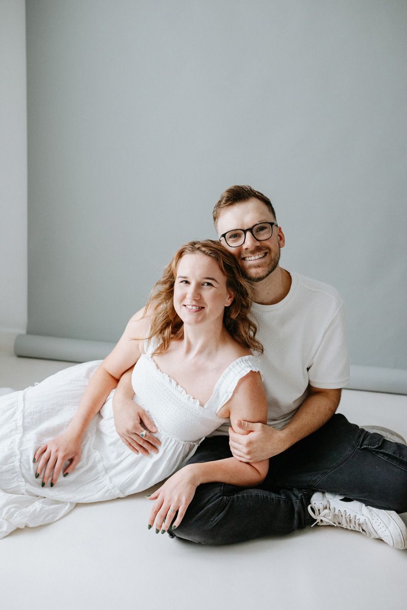 A couple in casual attire shares intimate moments while relaxing together on a white couch.