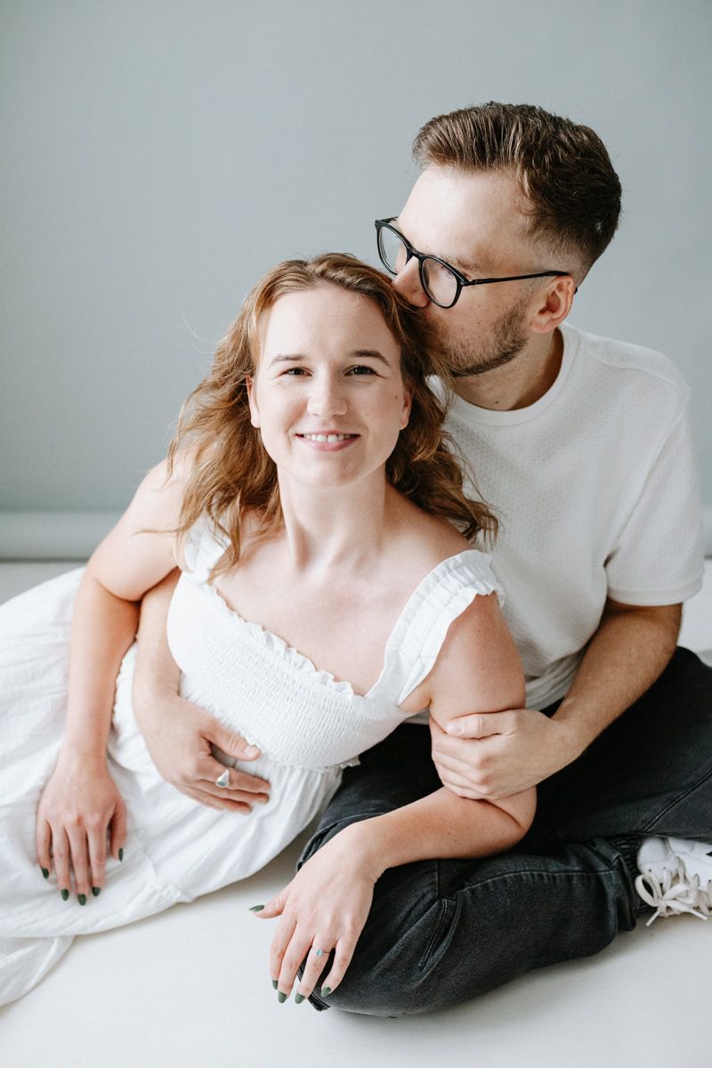 Intimate maternity photography series showing tender moments between expecting couple on white background.