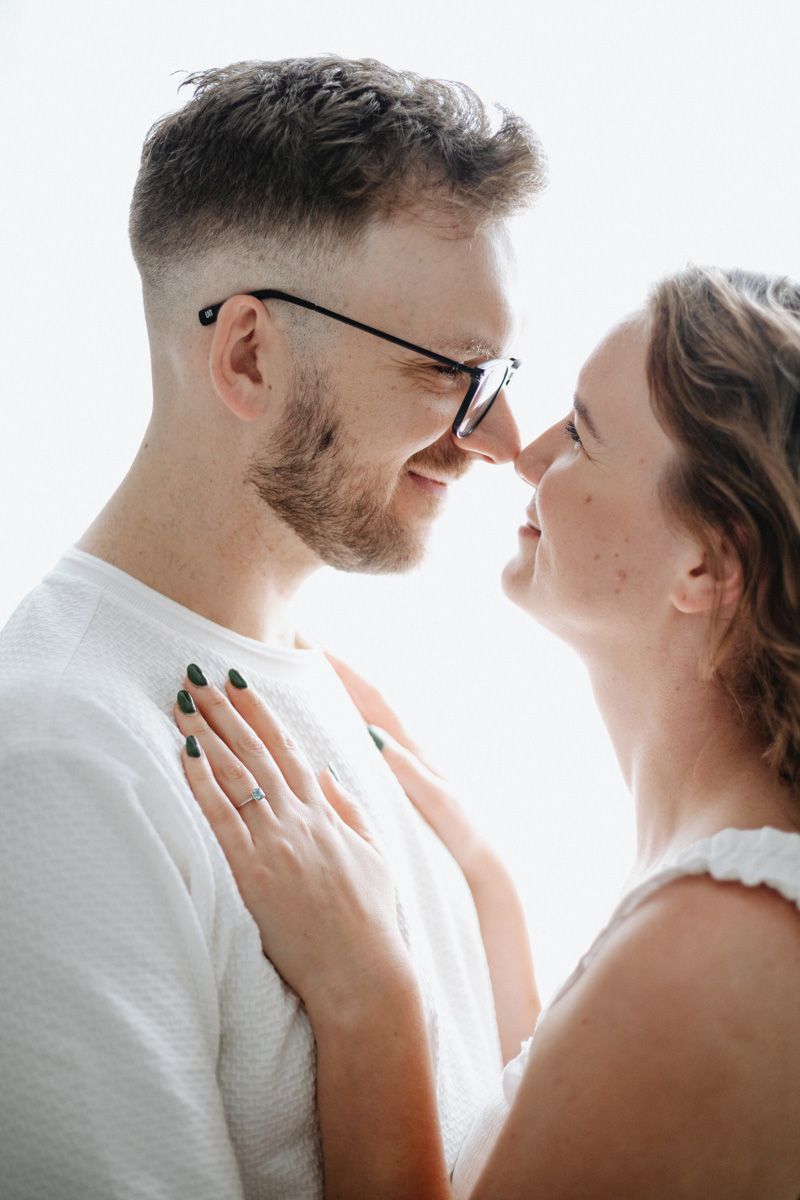 A romantic couple shares an intimate moment in a bright white setting, captured in a series of tender poses.