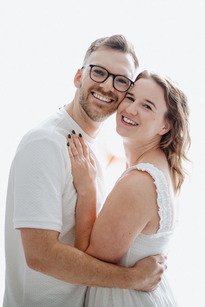 A happy couple embraces and laughs together in a bright white studio setting.