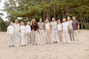 grote familie op zandverstuiving. alleen in wit/beige/bruine kleding op een lange rij naast elkaar.