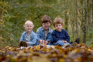 drie jongetjes tussen 2 en 4 jaar. zitten in een herfstbos. laag standpunt. jongetjes trekken gekke gezichten richting de camera.