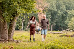 jong gezin wandelend in het bos. moeder zwanger. zoontje van 4. beide ouders houden een hand vast, zwaaien hem tussen hen in omhoog.