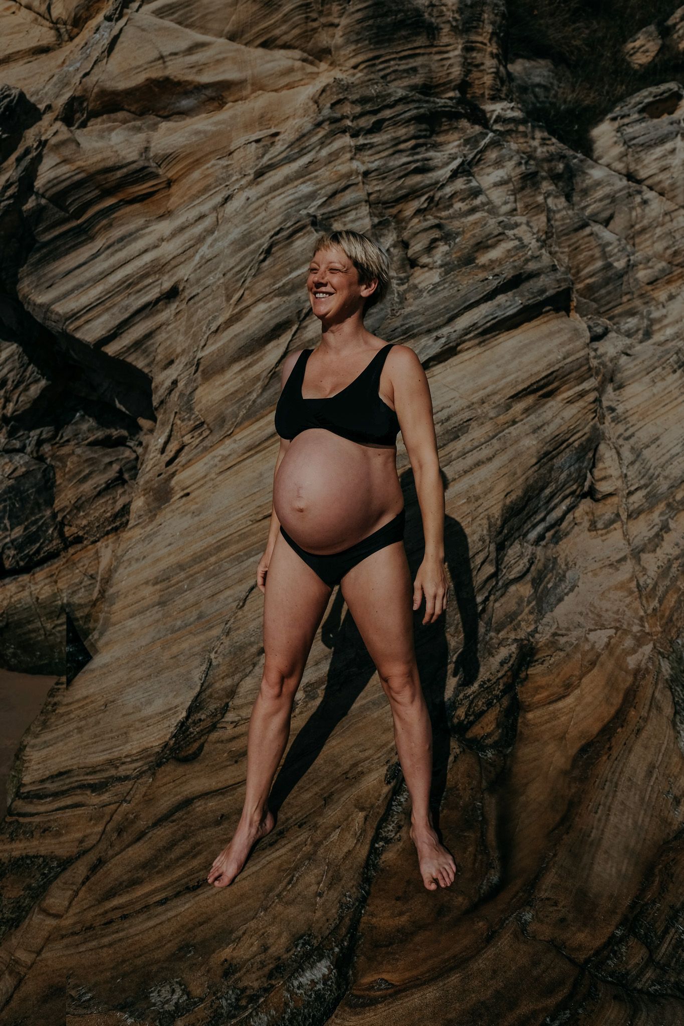 Outdoor maternity portrait of an expectant mother standing against coastal rock formations during a pregnancy photography session in Whitley