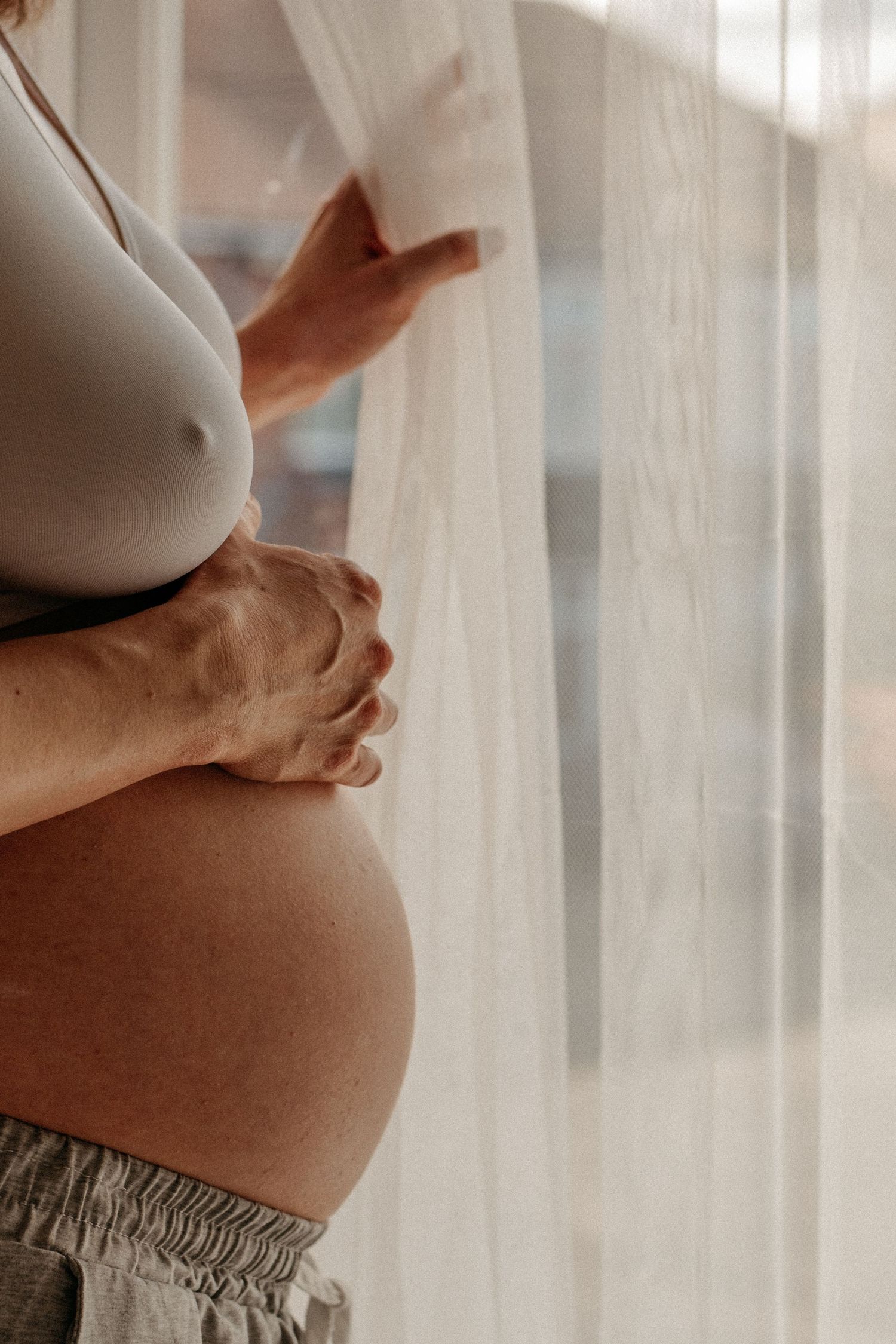Mother looking out of window holding pregnant belly in cullercoats