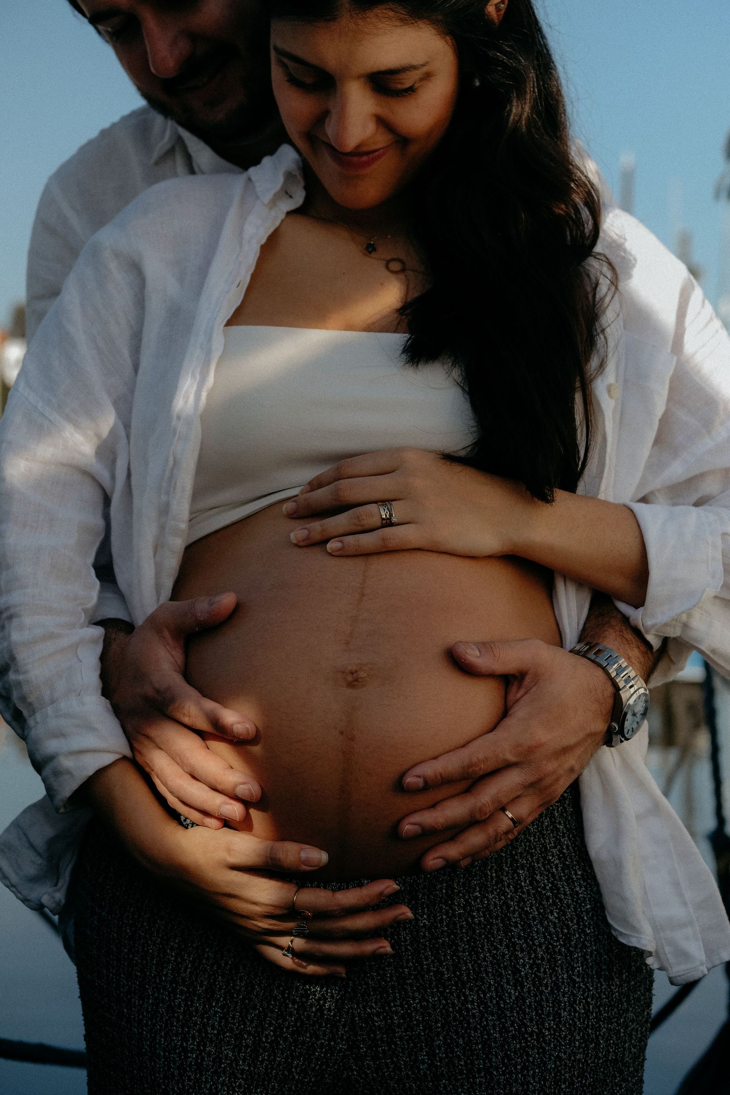 Expectant parents standing together outdoors with hands resting on a pregnant belly during a natural maternity photography session.