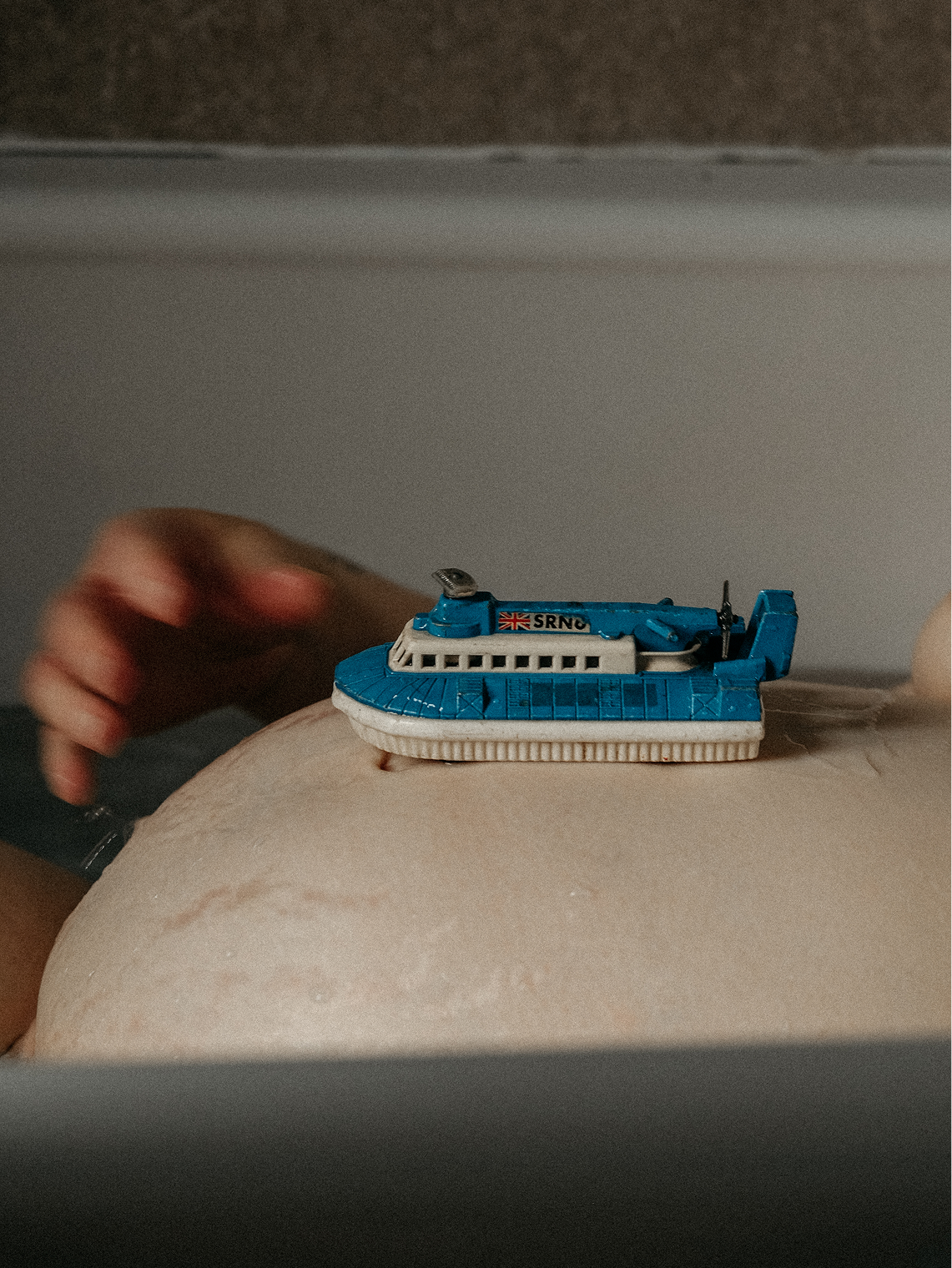 A woman playing with a toy boat on her pregnant belly in the bath in heaton during a pregnancy photoshoot