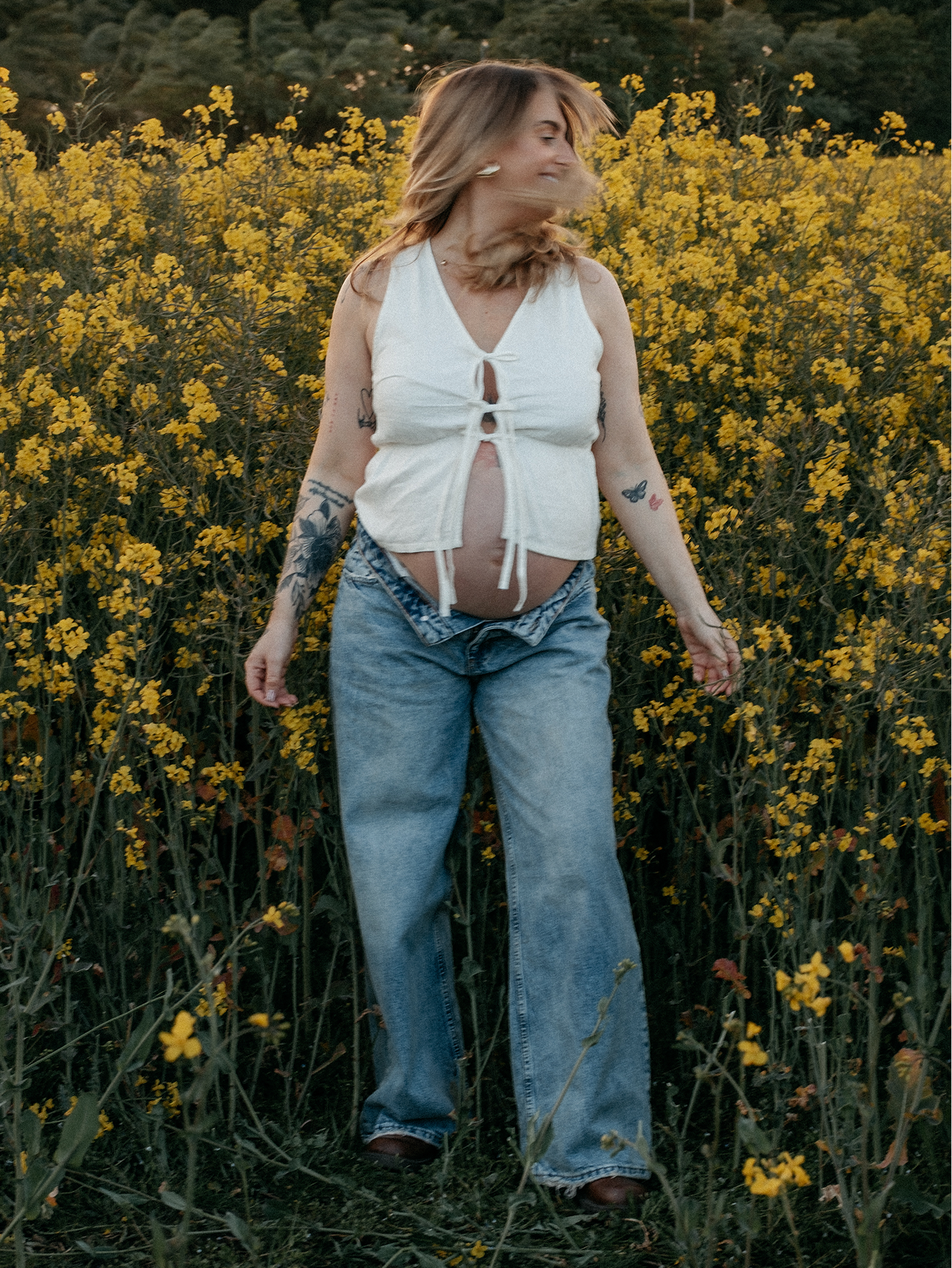 A woman laughing in a field of flowers in Sunderland with her pregnant belly