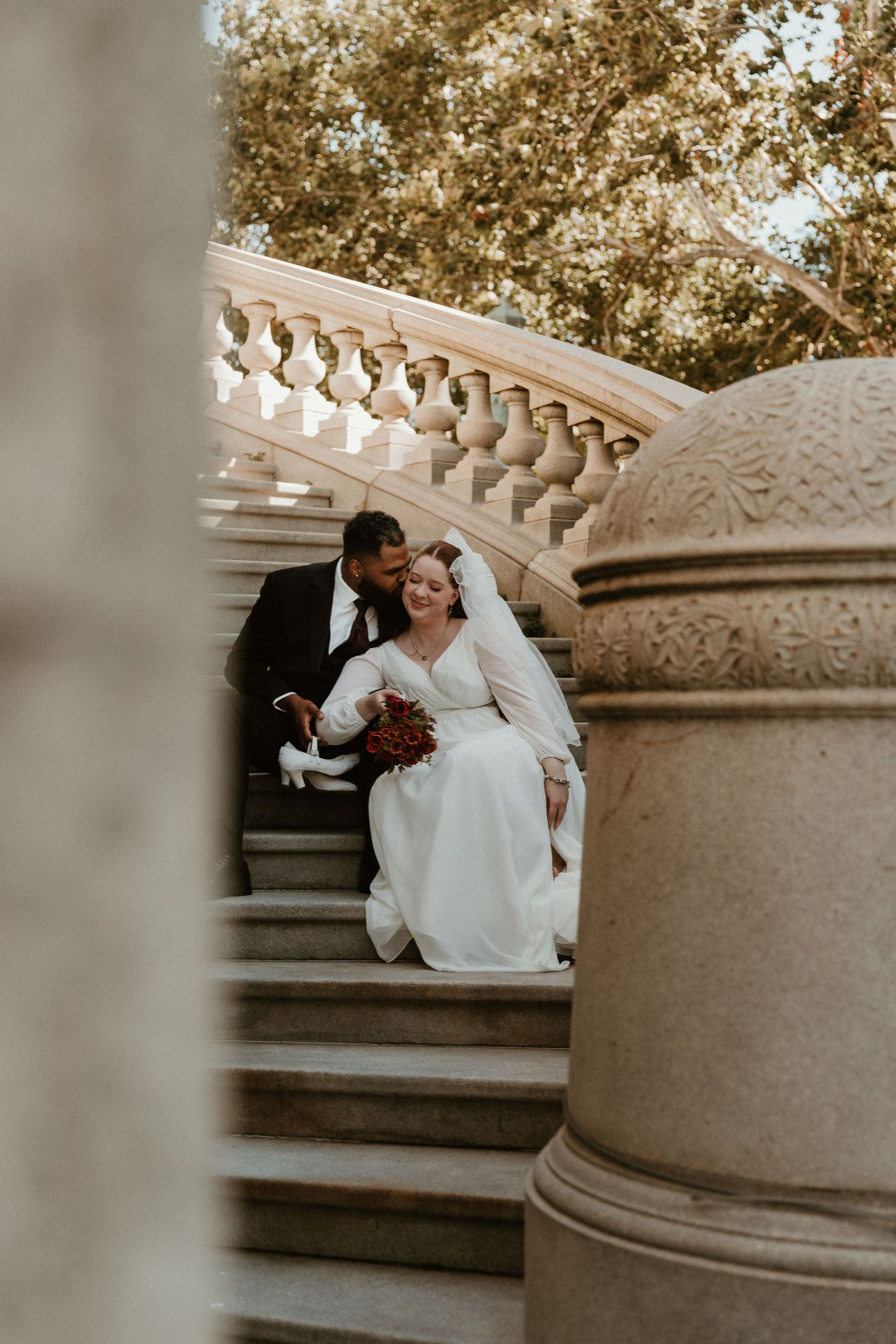 A couple sharing a joyful moment on ornate stone steps surrounded by foliage.