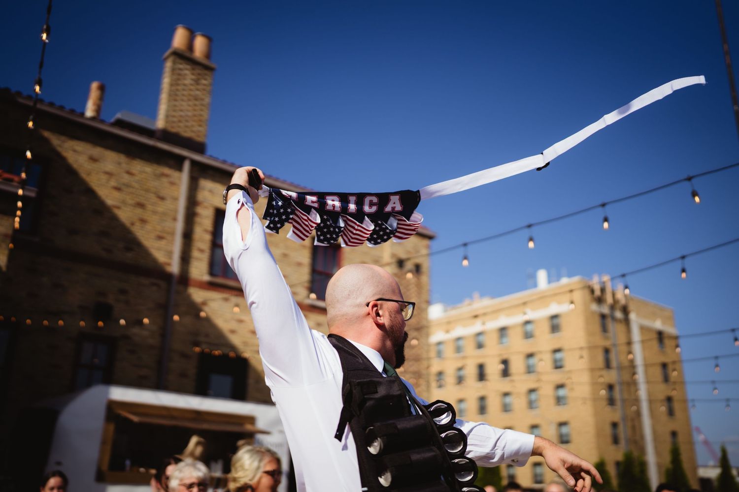 A joyful outdoor wedding celebration with string lights and historic brick buildings in the background.