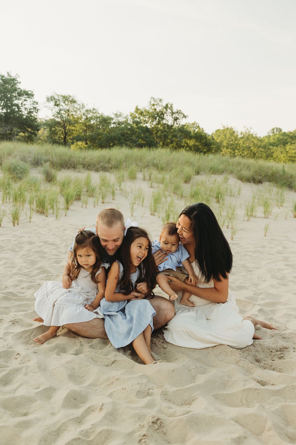 A family lounges together on a sandy beach during a warm summer evening photoshoot.