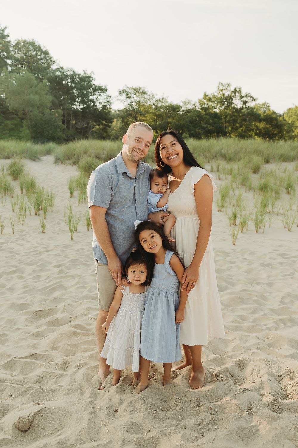 Family portrait session at a sandy beach with dunes and grass in the background during golden hour.