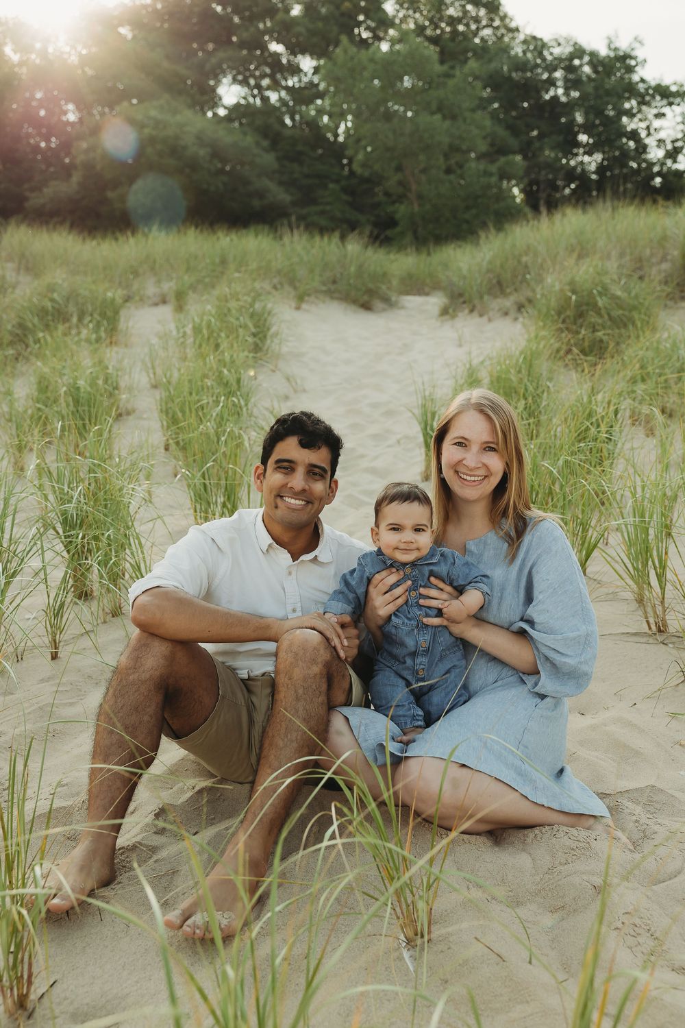 A family relaxes together on sandy beach dunes with tall grass on a sunny summer day.