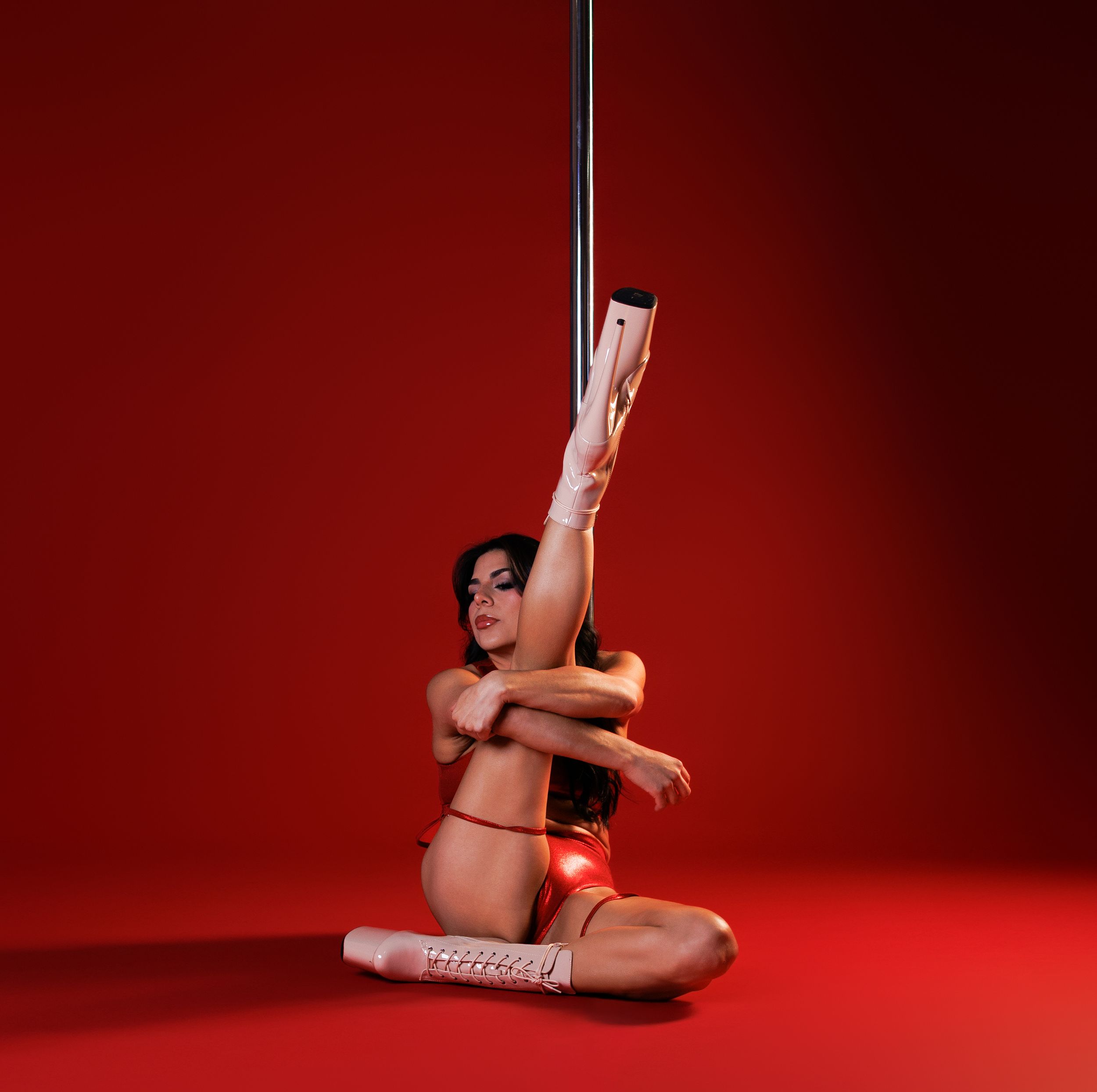 Dramatic pole dance silhouette against red backdrop showing athletic movement and flexibility.