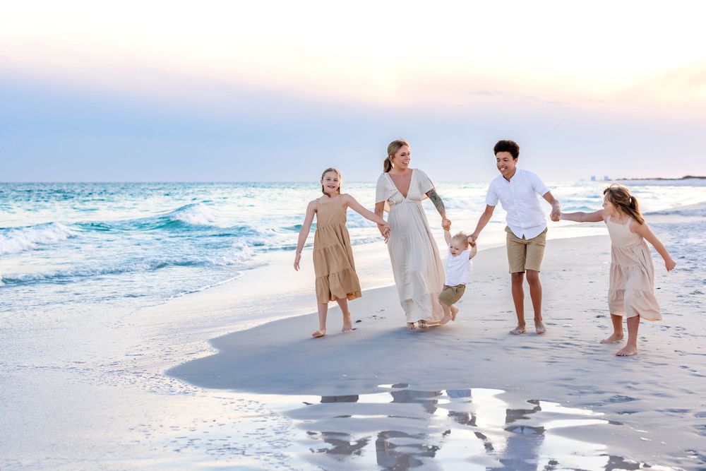 Family group walking together on white sandy beach at sunset wearing coordinated white and beige outfits.