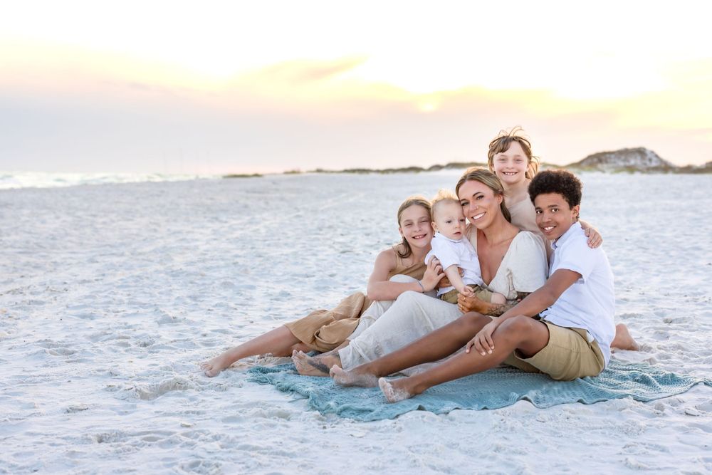 Family relaxing together on pristine beach shoreline during golden hour in coordinated casual attire.