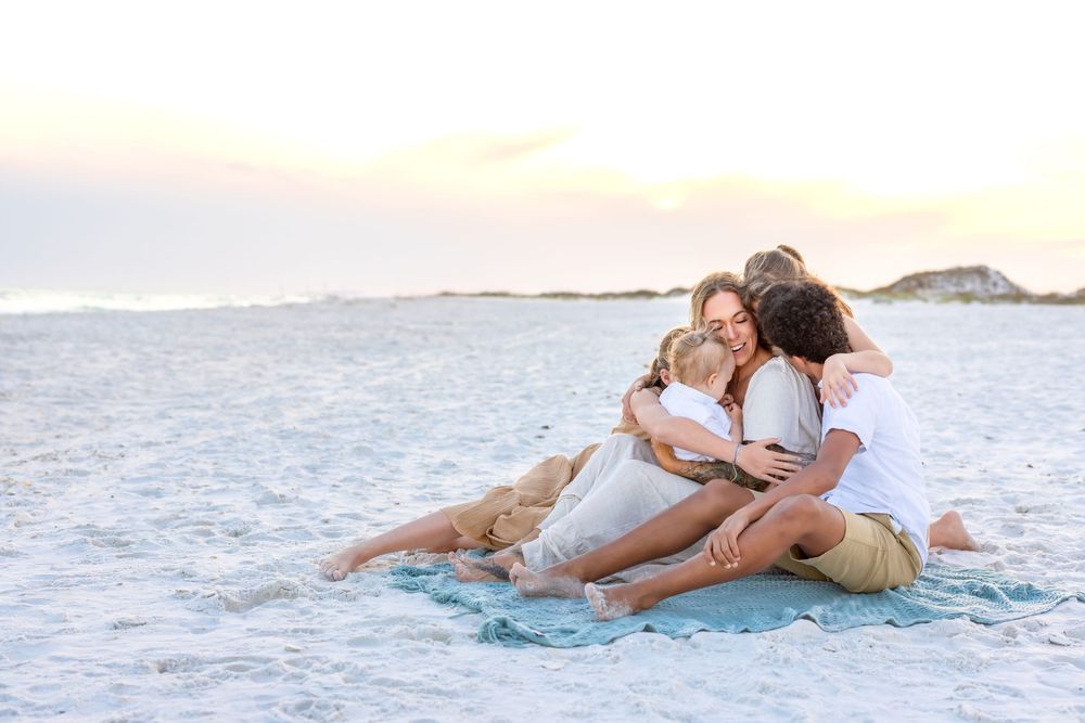 A couple relaxes together on a turquoise blanket by the ocean shore during golden hour.