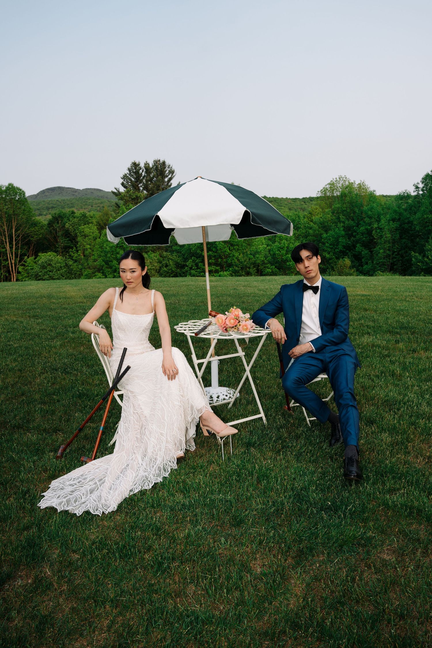 A couple sits in vintage chairs on a grassy field during a romantic outdoor photo session.