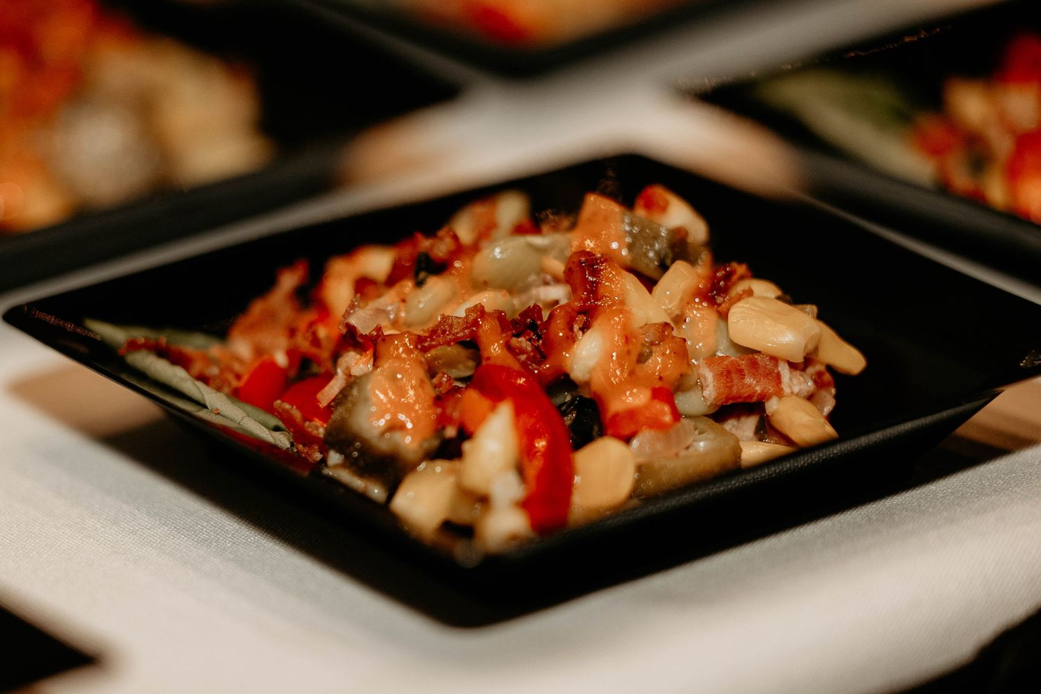 Diced vegetables and meat served in a black square plate with vibrant red sauce.
