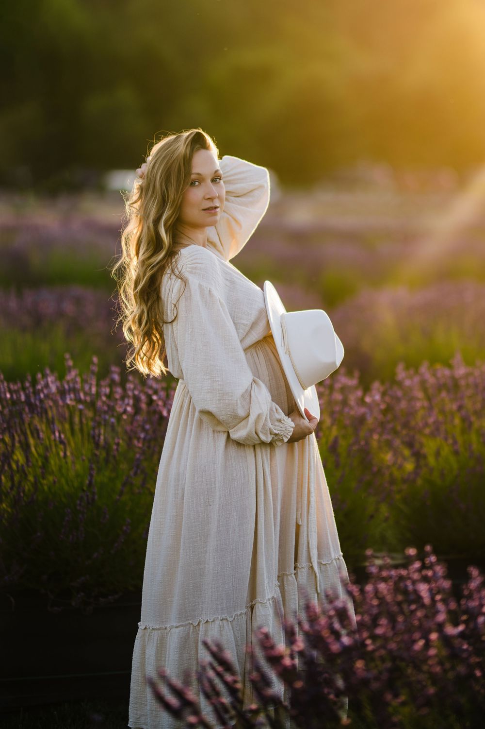A figure in a flowing white dress stands gracefully among blooming lavender fields at golden hour.