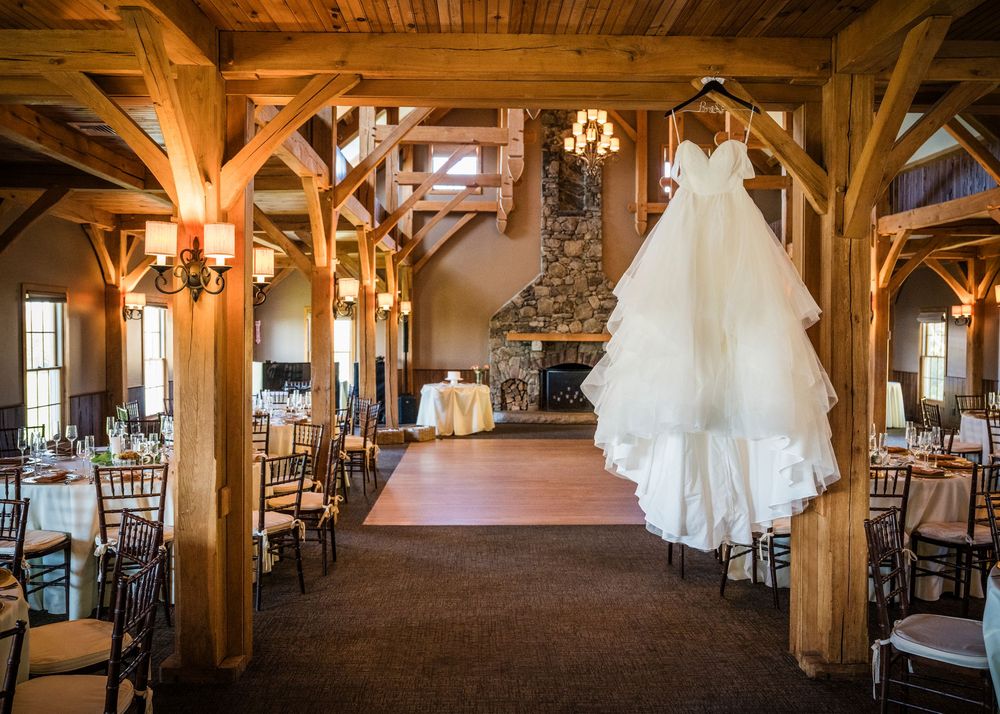 Rustic wooden beam interior of an elegant wedding venue with hanging white dress and warm lighting details.