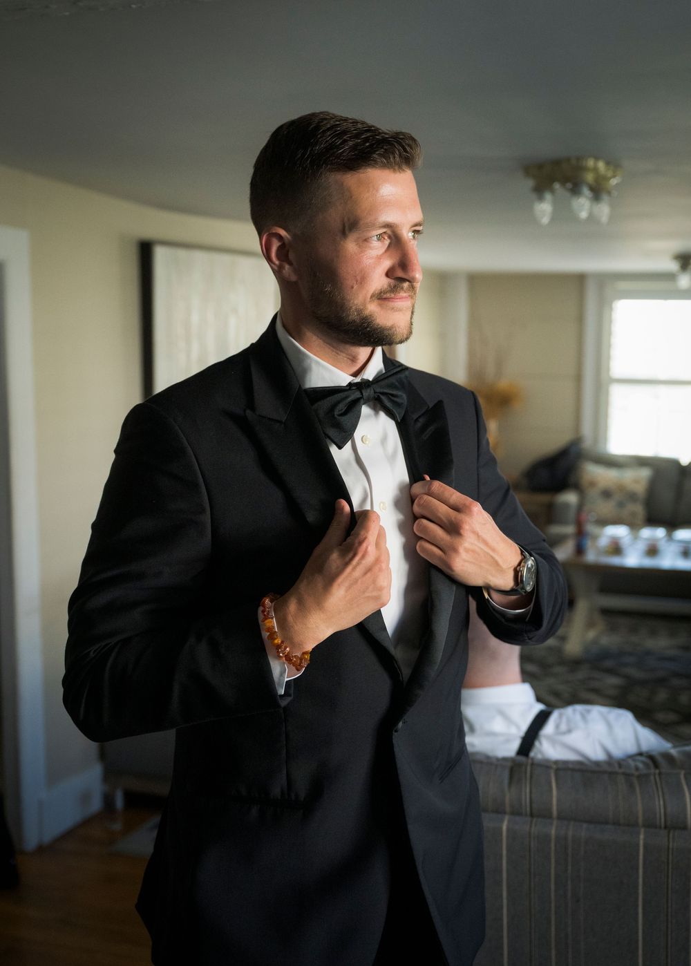 Series of elegant getting ready shots showing a groom adjusting his tie and suit in natural window light.