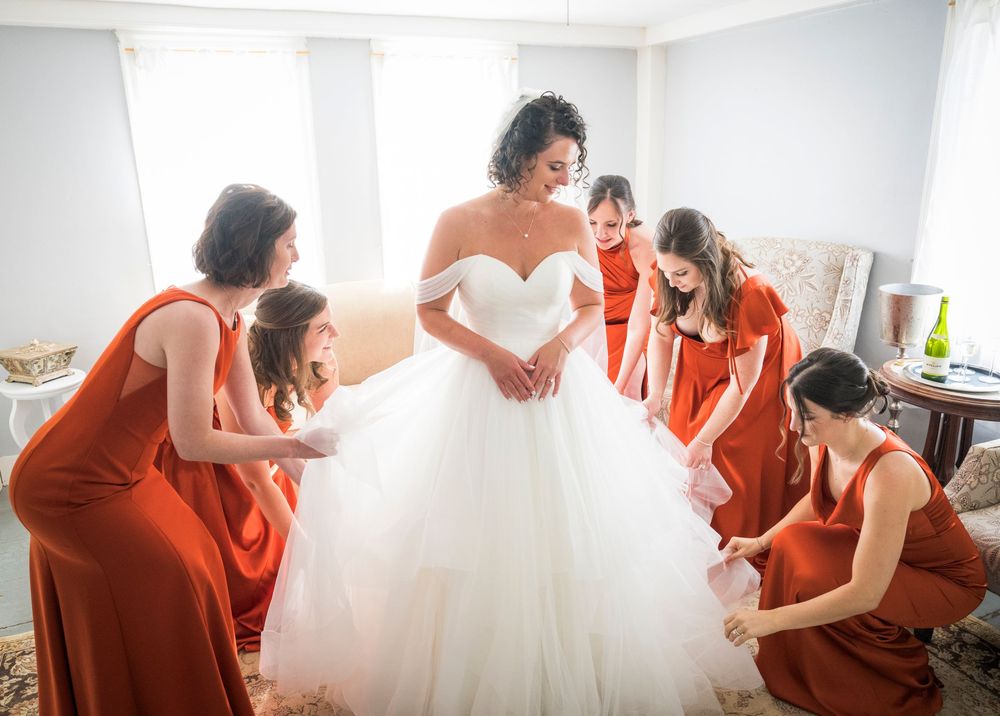 A sequence of photos showing a bride getting dressed in her wedding gown with help from her bridal party in red dresses.