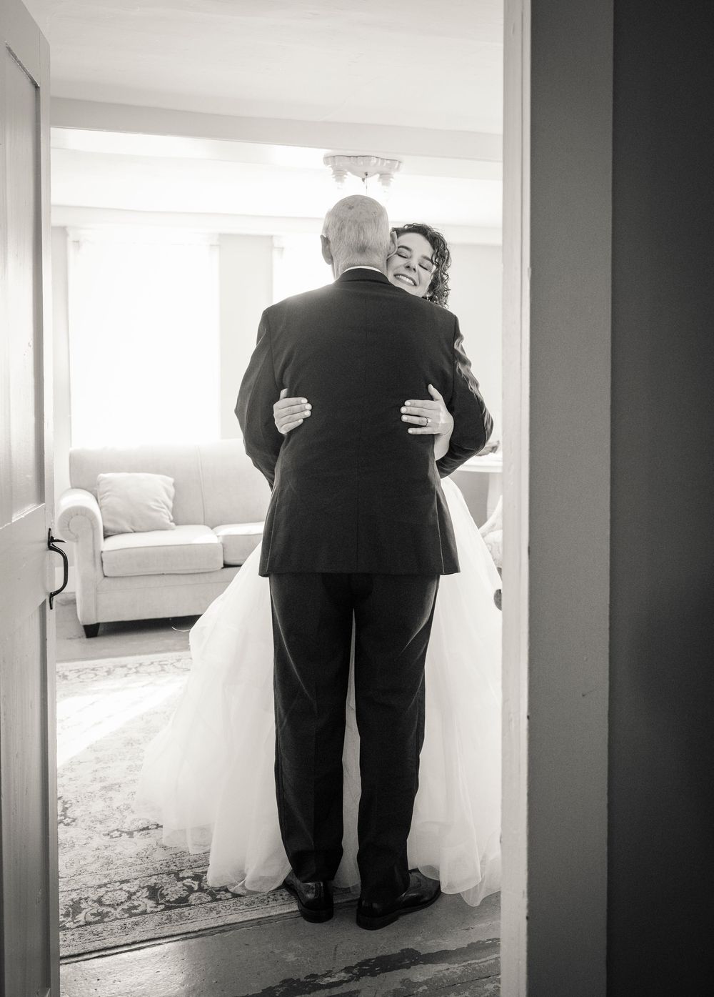 Black and white wedding photos showing intimate moments between family members embracing in a bright room.