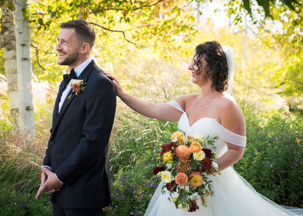 A couple shares a playful first look moment in a garden setting with autumn-colored florals.