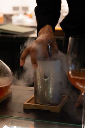 Smoke or vapor rises from a glass container being prepared at a dining table.