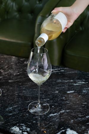 White wine being poured into an elegant wine glass on a dark marble surface.