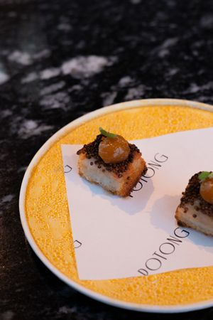 A sequence of seared food being plated on a white dish with yellow accents.