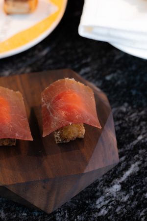 Close-up of sushi pieces with thin slices of raw fish arranged on a dark surface.