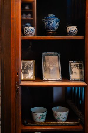 Display cabinet with blue and white porcelain dishes and picture frames on wooden shelves.