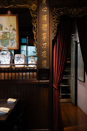 Traditional Asian interior with dark wood panels, gold lettering, and red curtains displaying artwork.