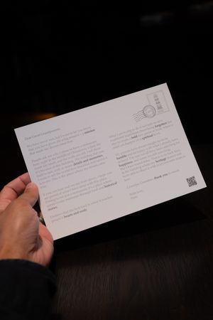 Hand holding a white paper document or receipt against a dark wooden surface.