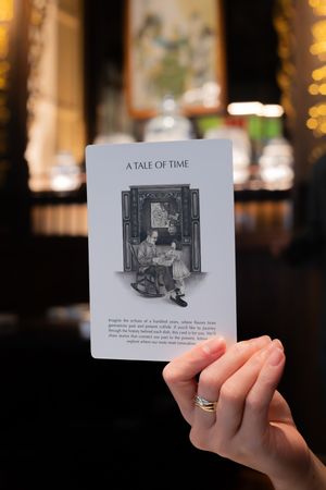 Hand holding a card titled 'A Tale of Time' featuring black and white illustrations.